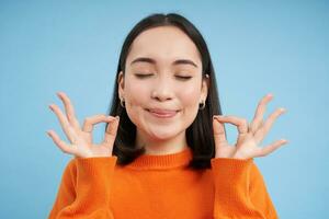 fechar acima do satisfeito sorridente ásia mulher, mostra OK, Está bem placa com satisfeito face, carrinhos sobre azul fundo foto