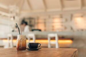 gelado café com leite e café café com leite caneca em de madeira mesa dentro restaurante e cafeteria com borrado cadeiras e contador debaixo natural luz foto