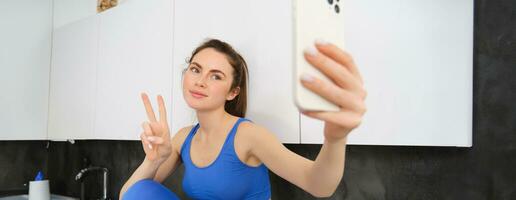 em forma e saudável jovem Esportes mulher, mostrando Paz sinal, levando selfie dentro roupas esportivas, ginástica blogueiro fazer fotos para social meios de comunicação dentro dela roupa ativa