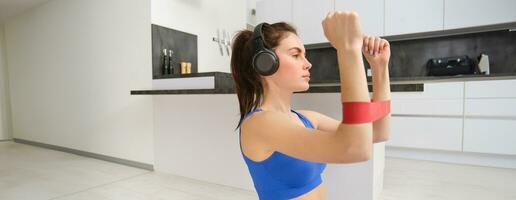 focado desportista exercite-se às lar, usando elástico resistência banda em braços, alongamento exercícios dentro vivo sala, aeróbica Treinamento foto