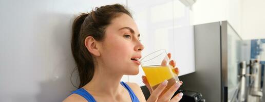 lindo mulher bebendo a orgânico laranja suco. em forma jovem mulher bebendo a partir de vidro. saudável menina apreciar desintoxicação beber e olhando longe foto