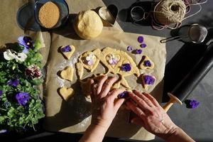 mulher com as mãos fazendo biscoitos em forma de coração com flor heartsease. foto