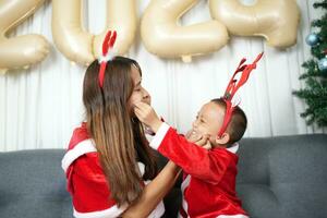 alegre Natal 2024 conceito mãe e criança decorar a Natal árvore com colorida Natal bolas. foto