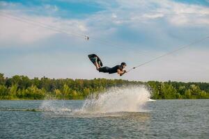 masculino praticante de wakeboard realizando pulando sobre água criando salpicos foto