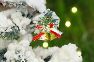 pequeno prata sinos aguentar em uma Natal árvore coberto dentro branco neve, sinalização este a feliz estação é chegando. foto