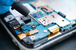 técnico que repara o interior do telefone móvel com o ferro de solda. circuito integrado. o conceito de dados, hardware, tecnologia foto