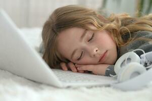 pequeno menina dormindo dentro dela cama dentro frente do a computador portátil foto