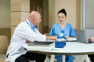 equipe do médico e enfermeira discutindo e debate em paciente médico registro depois de diagnóstico para preciso Cuidado plano com com experiência Senior médico especialista foto