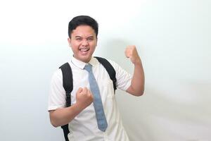 indonésio Senior Alto escola aluna vestindo branco camisa uniforme com cinzento gravata levantando dele punho, a comemorar sucesso. ganhando uma concorrência conceito. isolado imagem em branco fundo foto