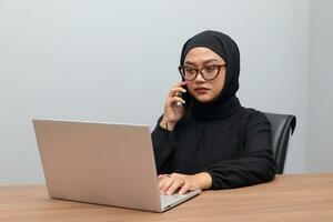 retrato do atraente ásia hijab mulher trabalhando em dela computador portátil. muçulmano menina fazer uma telefone ligar dentro escritório. empregado e freelance trabalhador conceito. foto