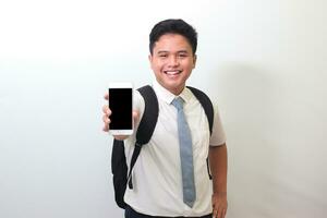 indonésio Senior Alto escola aluna vestindo branco camisa uniforme com cinzento gravata mostrando e apresentando em branco tela Móvel telefone. isolado imagem em branco fundo foto