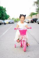 fofa pequeno ásia menina equitação uma bicicleta para exercício em a rua, crianças esporte e ativo estilo de vida foto