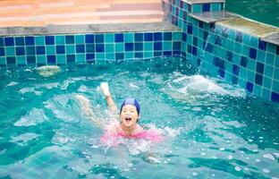 pequeno ásia menina vestindo inflável mangas jogando dentro a piscina foto