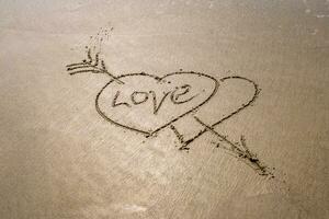 desenhando dentro areia dentro Formato do dois corações e inscrição amor foto
