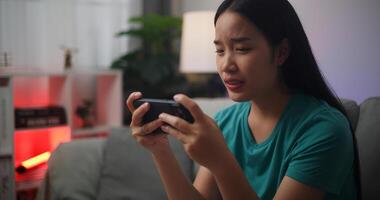 retrato do jovem ásia mulher sério jogando a conectados jogos frustrado com perda ou fracasso sentado em sofá dentro vivo quarto às home.gamer estilo de vida conceito. foto