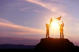 silhueta do homem de negocios liberando pombos em uma montanha pico com pôr do sol claro. conceito do Paz e liberdade símbolo do pensamento para o negócio foto