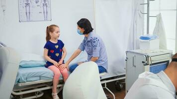 mãe com proteção mascarar reconfortante criança sentado dentro médico escritório durante COVID-19. médico especialista dentro remédio fornecendo saúde Cuidado Serviços tratamento consulta exame dentro hospital. foto