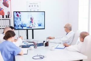 grupo do médicos ouvindo médico especialista durante vídeo ligar dentro conferência sala. remédio funcionários usando Internet durante conectados encontro com especialista médico para perícia. foto