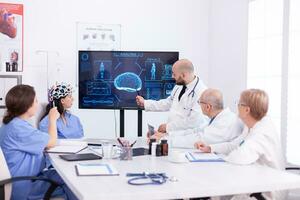 médico falando sobre cérebro atividade durante conferência com médico funcionários e enfermeira vestindo fone de ouvido com sensores. monitor mostra moderno cérebro estude enquanto equipe do cientista ajusta a dispositivo. foto