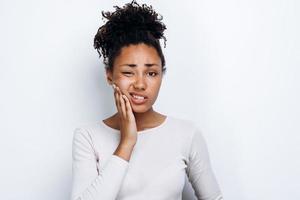 garota afro-americana em pé sobre um fundo branco isolado tocando a boca com a mão com uma expressão dolorida por causa de uma dor de dente foto