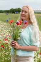 lindo meia idade Loiras mulher carrinhos entre uma floração campo do papoilas foto