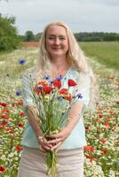 lindo meia idade Loiras mulher carrinhos entre uma floração campo do papoilas foto