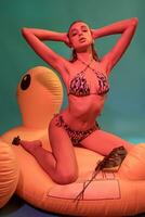 delgado menina dentro bikini sentado em inflável colchão tocante cabelo com mãos foto