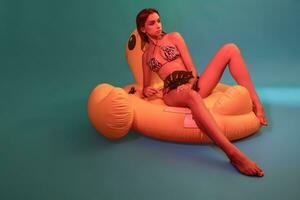 delgado mulher dentro bikini com monstera folha sentado em inflável piscina flutuador foto