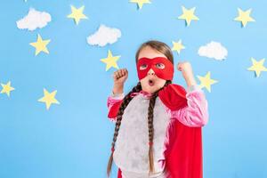 pequeno criança tocam Super heroi. criança em a fundo do brilhante azul parede com branco nuvens e estrelas . menina poder conceito. foto