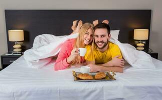 feliz jovem casal tendo café da manhã bandeja em cama às casa foto