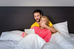 jovem doce casal às cama assistindo alguma coisa em tábua gadget foto