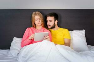 jovem doce casal às cama assistindo alguma coisa em tábua gadget foto