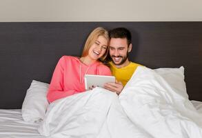 jovem doce casal às cama assistindo alguma coisa em tábua gadget foto