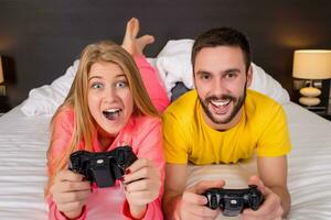 feliz jovem casal tendo Diversão jogando videogames dentro cama foto