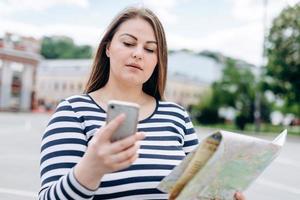 turista feminina com smartphone e mapa de papel nas mãos, procurando direção ao ar livre