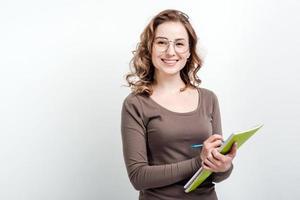 garota atraente de óculos faz anotações no livro de exercícios em um fundo branco foto