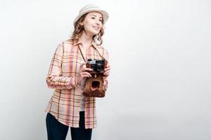 garota com câmera retro e chapéu desvia o olhar no fundo da parede branca foto