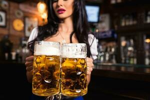 jovem sexy oktoberfest garçonete, vestindo uma tradicional bávaro vestir, servindo grande Cerveja canecas às bar. foto