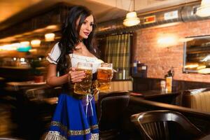 lindo fêmea garçonete vestindo tradicional dirndl e segurando enorme cervejas dentro uma bar. foto