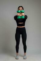 desportivo menina realizando ombro exercícios com halteres em cinzento fundo foto