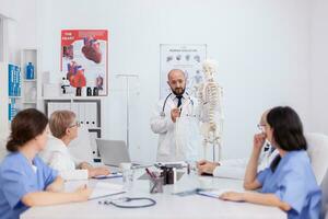 médico médico com estetoscópio segurando mão osso explicando corpo humano esqueleto apresentando anatomia estrutura discutindo médico perícia. hospital equipe trabalhando dentro conferência encontro quarto foto