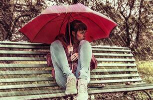 jovem mulher abrigo a partir de a outono chuva com uma vermelho guarda-chuva foto