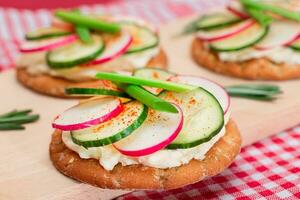 luz café da manhã ou dieta comendo crocantes biscoito sanduíche com creme queijo, fresco pepino, verde cebolas e rabanete em de madeira cozinhando borda em magenta fundo foto