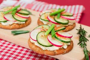 luz café da manhã ou dieta comendo crocantes biscoito sanduíche com creme queijo, fresco pepino, verde cebolas e rabanete em de madeira cozinhando borda em magenta fundo foto