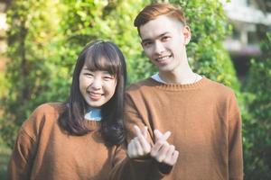 lindo casal jovem fazendo formato de coração com as mãos e sorrindo feliz e apaixonado ao ar livre foto