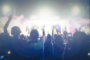 silhuetas da multidão do show em vista traseira da multidão do festival levantando as mãos nas luzes brilhantes do palco foto