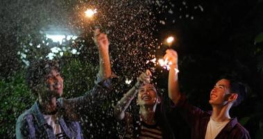 Grupo asiático de amigos fazendo churrasco ao ar livre no jardim, rindo com bebidas alcoólicas de cerveja e mostrando um grupo de amigos se divertindo com estrelinhas à noite, foco suave foto