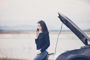 Mulher asiática usando telefone celular enquanto olha e homem estressado sentado após uma quebra de carro na rua foto