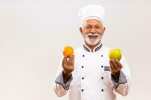 retrato do Senior chefe de cozinha mostra fruta em cinzento fundo. foto
