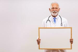 retrato do Senior médico segurando quadro branco em cinzento fundo. foto